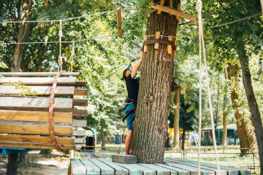 Küçük mutlu çocuk güneşli bir yaz gününde tırmanış parkında eğleniyor.