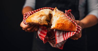 Yeni pişmiş ekmeği elinde tutan fırıncının kırpılmış görüntüsü.