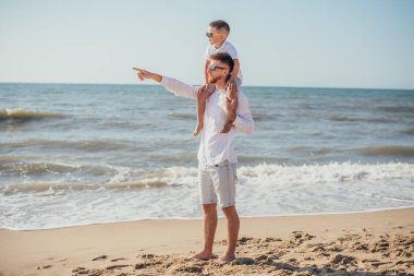 Mutlu genç baba yaz vakti kumlu sahilde boynunu tutuyor.