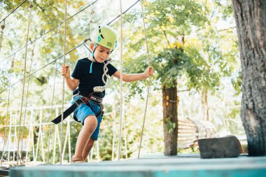 Güneşli bir yaz gününde tırmanış parkında eğlenen sevimli, gülümseyen bir çocuk.