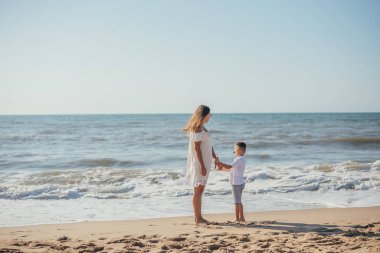 Kumsalda bir arada duran küçük tatlı oğlu olan genç annenin yan görüntüsü.