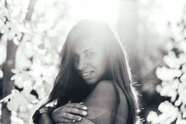 Açık havada poz veren ve güneşli bir günde kameraya gülümseyen güzel bir genç kadının siyah beyaz görüntüsü.