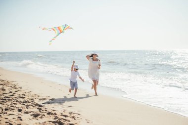 Mutlu anne ve oğul kumsalda renkli uçurtmayla oynuyorlar.