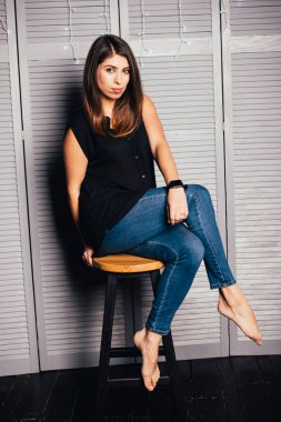 Giyim kuşamında güzel genç bir kadın oturuyor ve içeride kameraya bakıyor.   