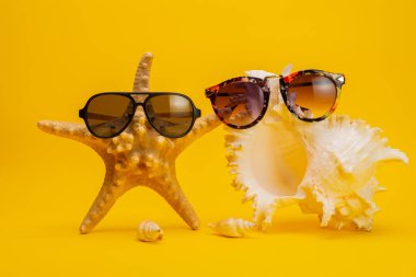 Sarı arka planda deniz yıldızı, güneş gözlüğü ve deniz kabuklarının yakın plan görüntüsü, tatil konsepti  