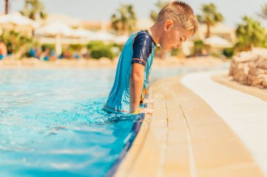 Yaz tatilinde havuzda yüzen sevimli küçük çocuğun yan görüntüsü.  