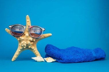 Yakın plan deniz yıldızı, güneş gözlüğü ve deniz kabuğu manzarası ve mavi arka plan havlusu, tatil konsepti  