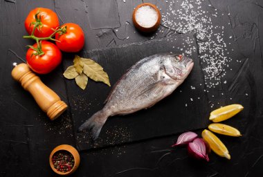 Taze balıkların, domateslerin, limon dilimlerinin, soğan ve körfez yapraklarının üst görüntüsü.