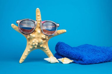 Yakın plan deniz yıldızı, güneş gözlüğü ve deniz kabuğu manzarası ve mavi arka plan havlusu, tatil konsepti  