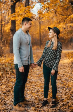 Güzel mutlu genç çift el ele tutuşup sonbahar parkında yürüyor.