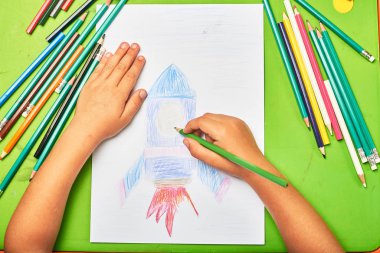 Küçük çocuk masada kalemle roket çiziyor.