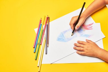 Küçük çocuk masada kalemle roket çiziyor.