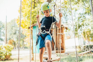 Küçük şirin çocuk yaz güneşli bir günde tırmanış parkında eğleniyor.