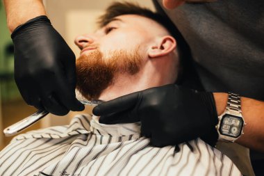 Berber dükkanındaki adama sakal tıraşı olurken çekilmiş bir fotoğraf.