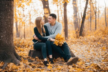 Güzel mutlu genç çift sonbahar ormanında birlikte oturuyor.