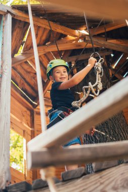 Küçük mutlu çocuk güneşli bir yaz gününde tırmanış parkında eğleniyor.