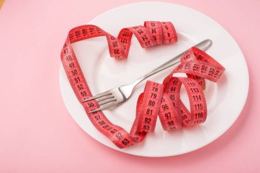 Pembe zemin üzerinde çatal ve mezurayla beyaz plakanın yakın plan görüntüsü