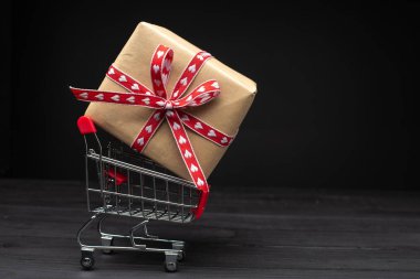 Koyu ahşap arka planda alışveriş arabası ve hediye kutusu. 
