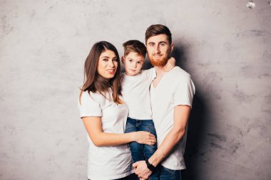 Mutlu, genç ebeveynler küçük sevimli bir oğlan taşıyor ve kameraya gülümsüyor.