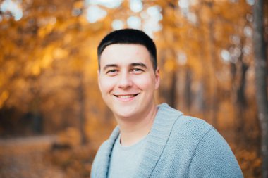 Sonbahar ormanında kameraya gülümseyen yakışıklı genç adamın portresi.