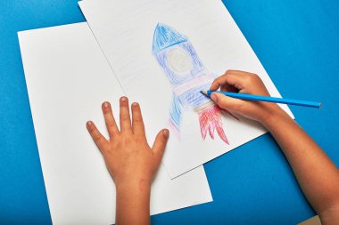 Küçük çocuk masada kalemle roket çiziyor.