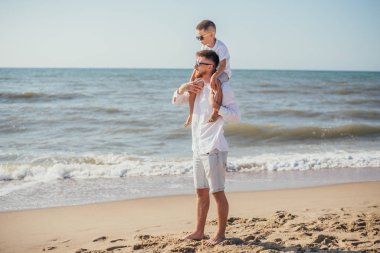 Mutlu genç baba yazın sahilde boynu çok sevimli küçük oğlunu taşıyor.