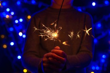 Noel arkaplanında elinde yanan maytap, kesilmiş mermi tutan bir çocuk var.