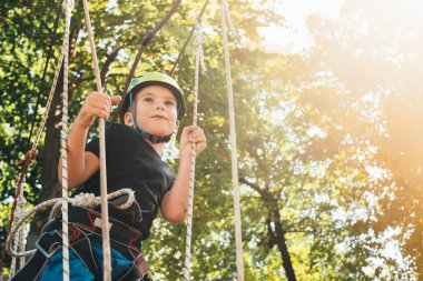Sevimli mutlu çocuk güneşli bir günde macera parkında eğleniyor.