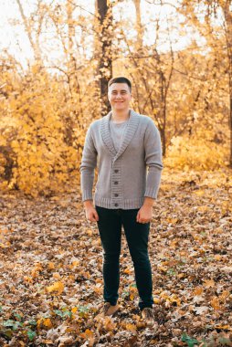 Sonbahar parkında kameraya bakıp gülümseyen yakışıklı, neşeli genç adam manzarası.