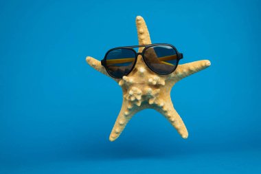 Mavi arka planda güneş gözlüklü deniz yıldızının yakın plan görüntüsü, tatil konsepti  