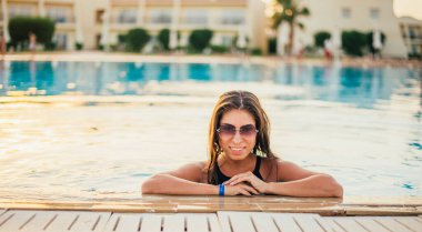 Yüzme havuzunda dinlenen mayo ve güneş gözlüklü genç bayan dinleniyor.