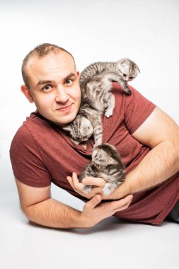 Yakışıklı, gülümseyen genç adam beyaz arka planda sevimli tüylü kedilerle oynuyor.
