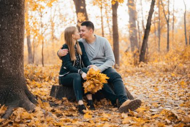 Güzel mutlu genç çift birlikte oturup sonbahar ormanında öpüşüyor.