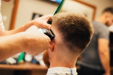 Genç bir adamın berber dükkanında profesyonel elektrikli makasla kırpılırken çekilmiş bir fotoğrafı. 