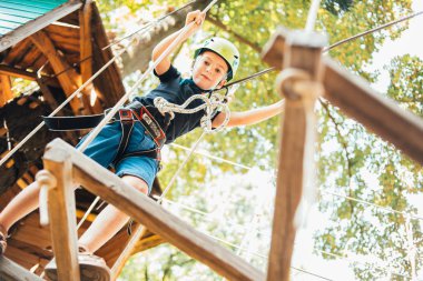Küçük şirin çocuk yaz güneşli bir günde tırmanış parkında eğleniyor.