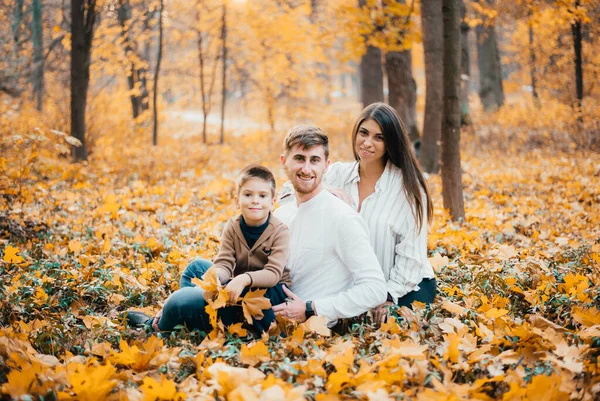 秋の公園に1人の子供と一緒に座っている美しい幸せな若い家族 — ストック写真