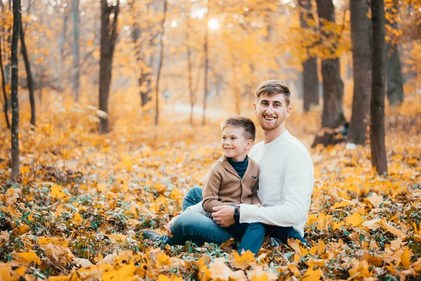 happy father with son sitting together in autumn park