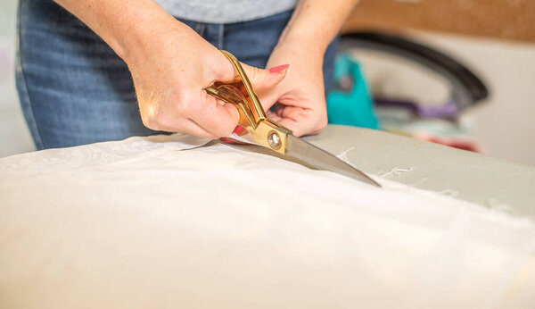 Partial view of seamstress cutting fabric with scissors and making a garment in workplace