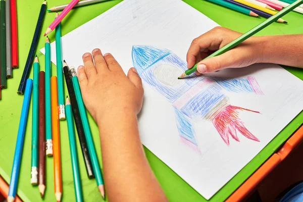 Küçük çocuk masada kalemle roket çiziyor.