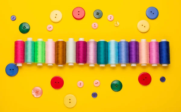 top view of colorful sewing threads and buttons on yellow background