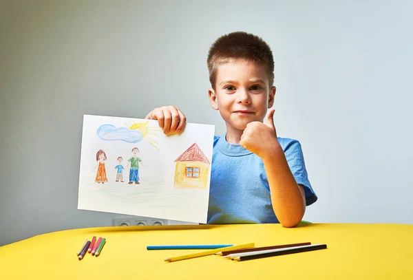小男孩在桌旁用铅笔画家庭和房子 — 图库照片