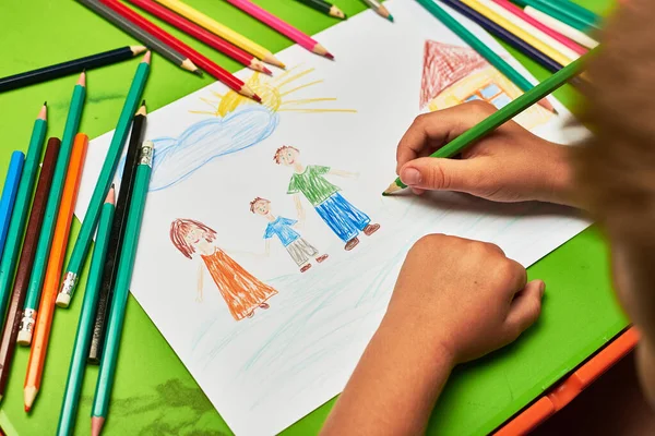 little boy drawing family and house by pencil at table