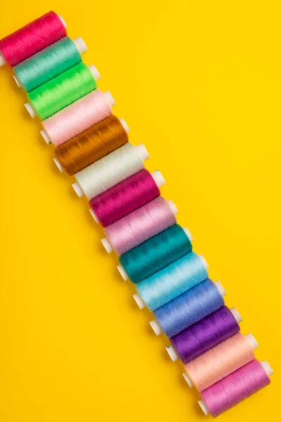 top view of colorful sewing threads on yellow background