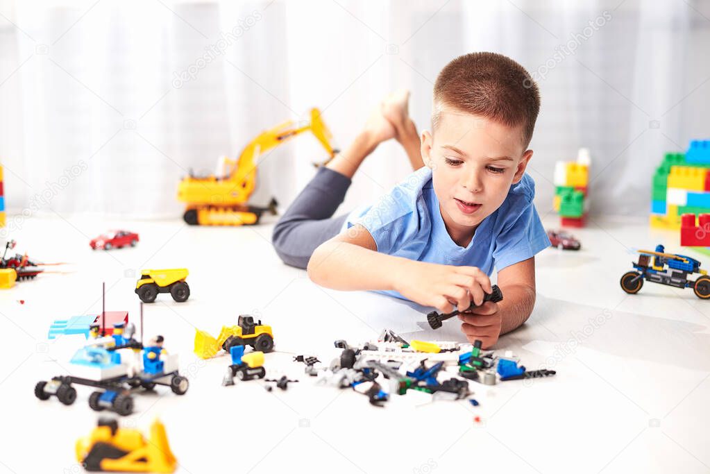 adorable little boy lying on floor and playing with construction plastic toy blocks 