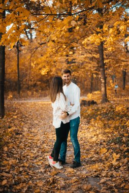 Mutlu genç çift, sonbahar ormanında ayakta ve sarılıyorlar.