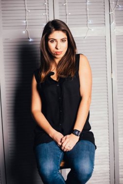 Giyim kuşamında güzel genç bir kadın oturuyor ve içeride kameraya bakıyor. 