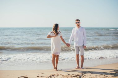 Mutlu genç çift el ele tutuşuyor ve kumsalda birlikte duruyorlar. 