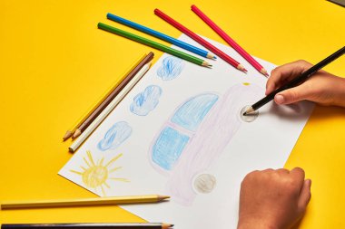 Küçük çocuk masada kurşun kalemle araba çiziyor.