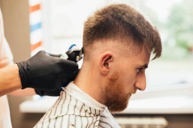 Genç adam berber dükkanında profesyonel elektrikli makasla kırpılıyor. 