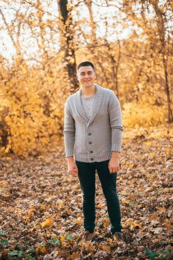 Sonbahar parkında kameraya bakıp gülümseyen yakışıklı, neşeli genç adam manzarası.